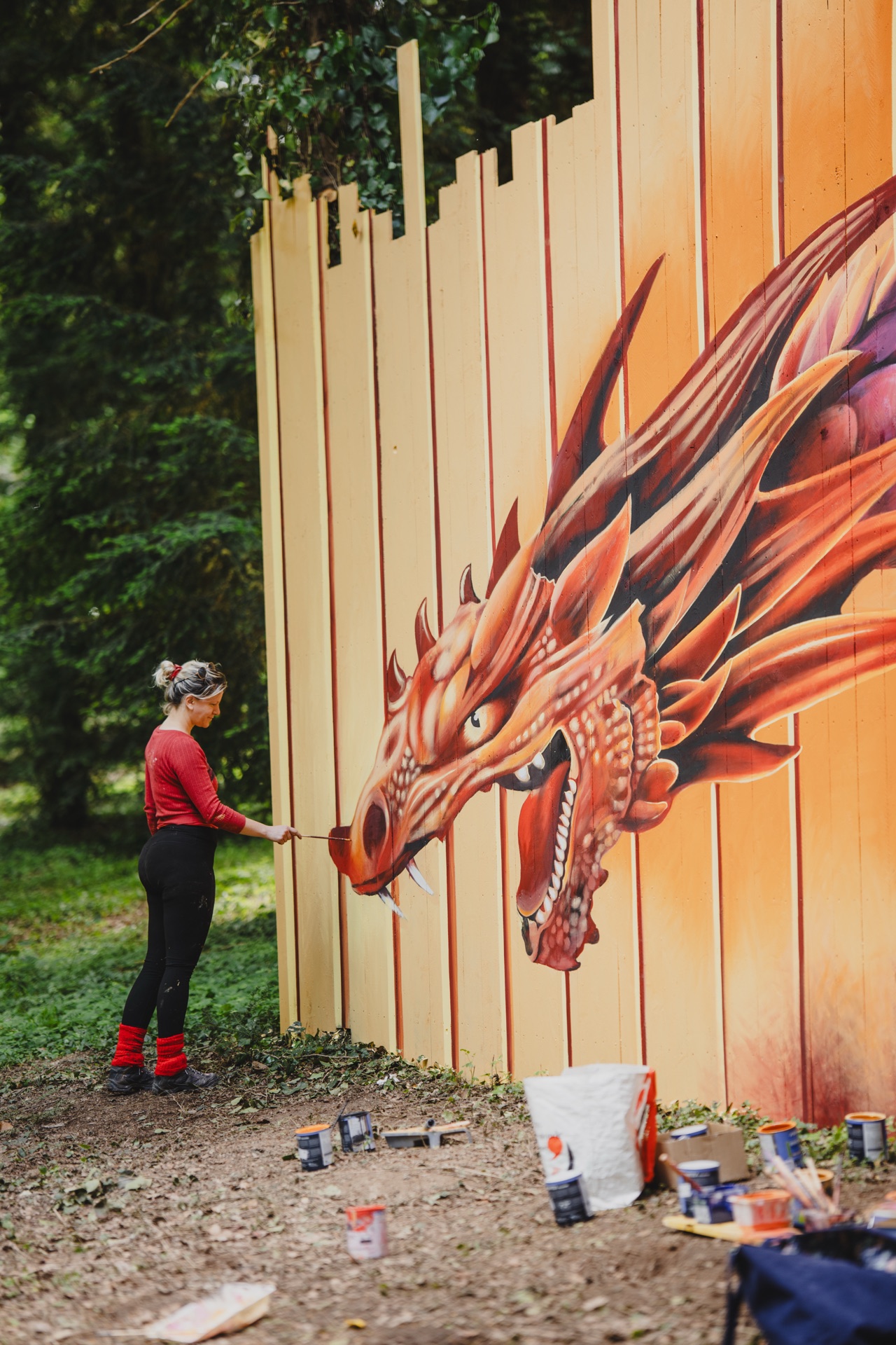 Une artiste peint un dragon monumental sur une palissade dans le parc