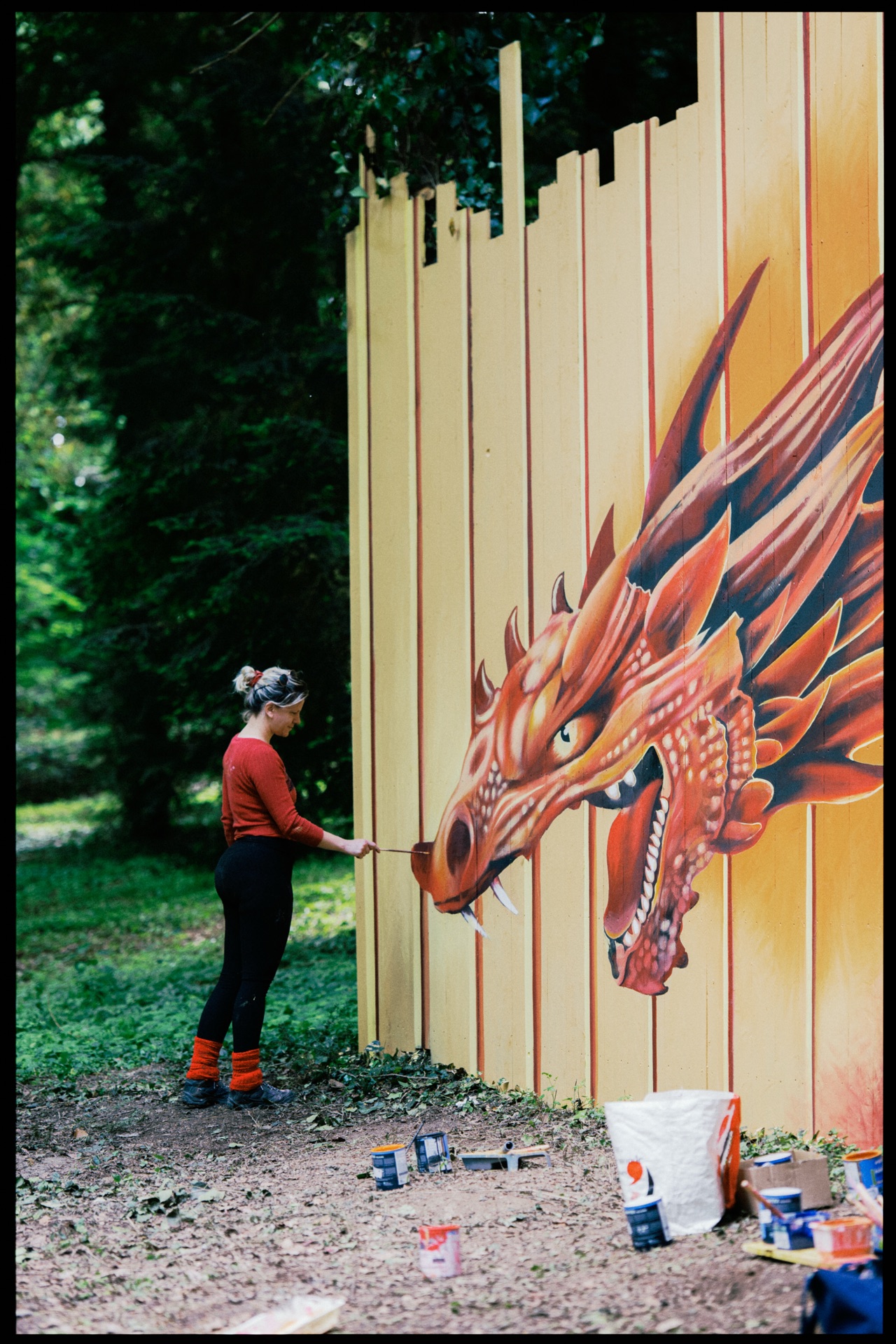 An artist painting a dragon on a fence among the trees
